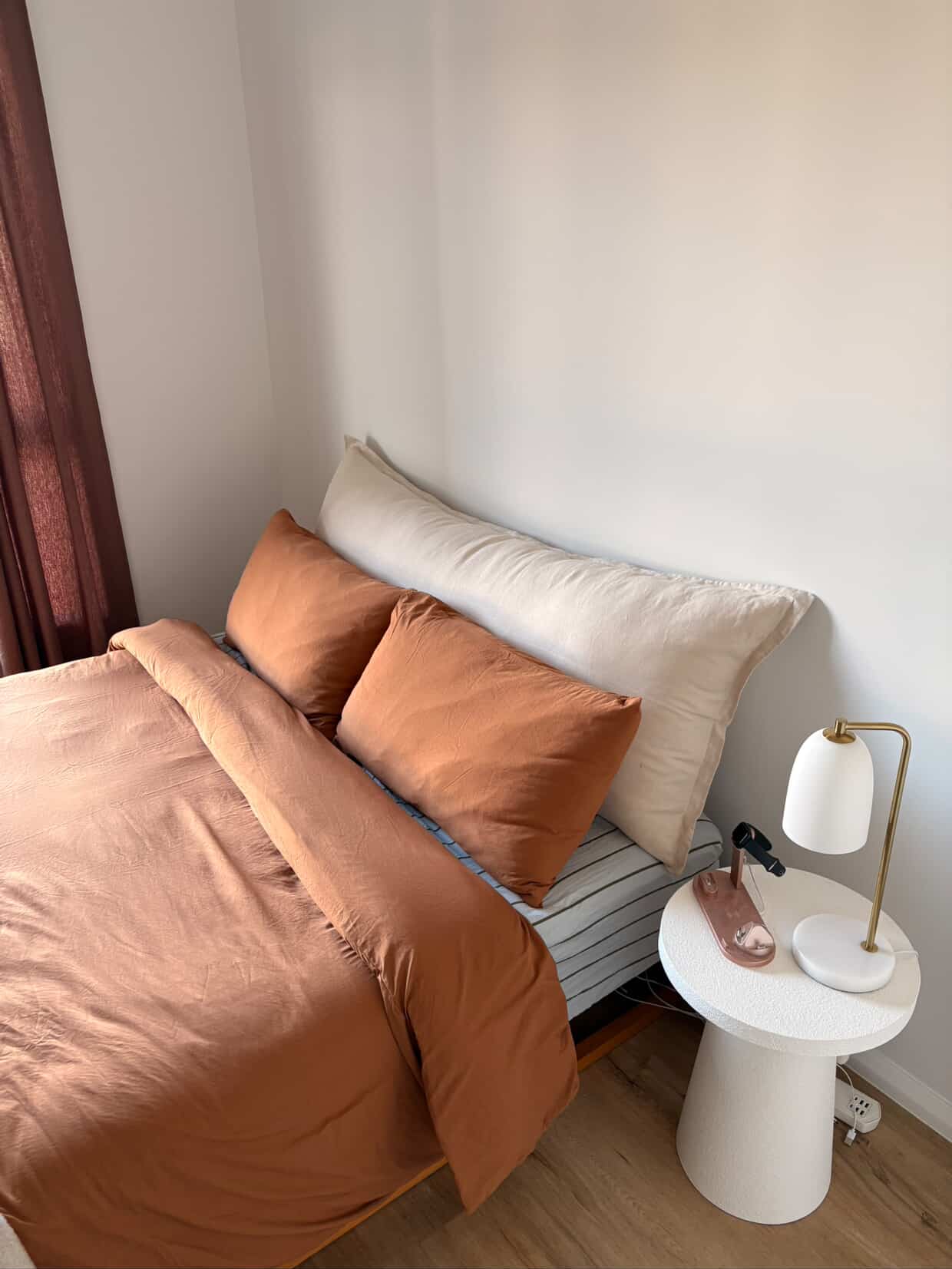 Stone linen bedhead cushion with brass bedside lamp and rust curtains