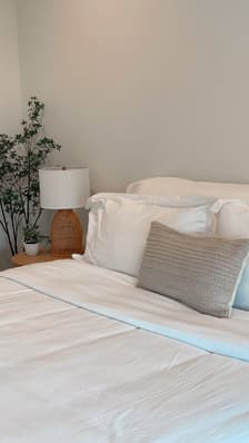 Natural linen bedhead cushion in guest bedroom with soft lighting and potted plant